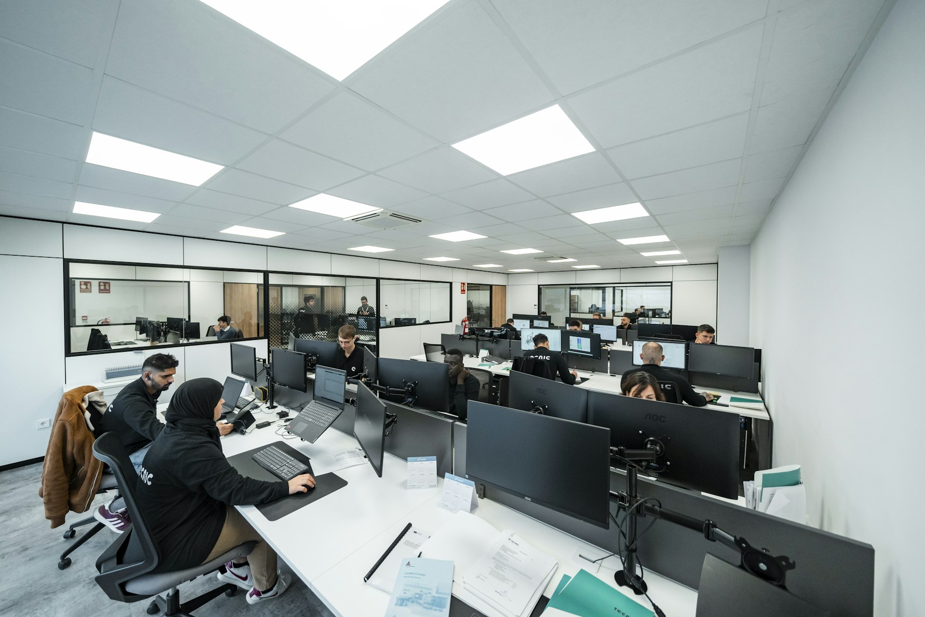 People working at computers on an operations floor, with documents on the desks.